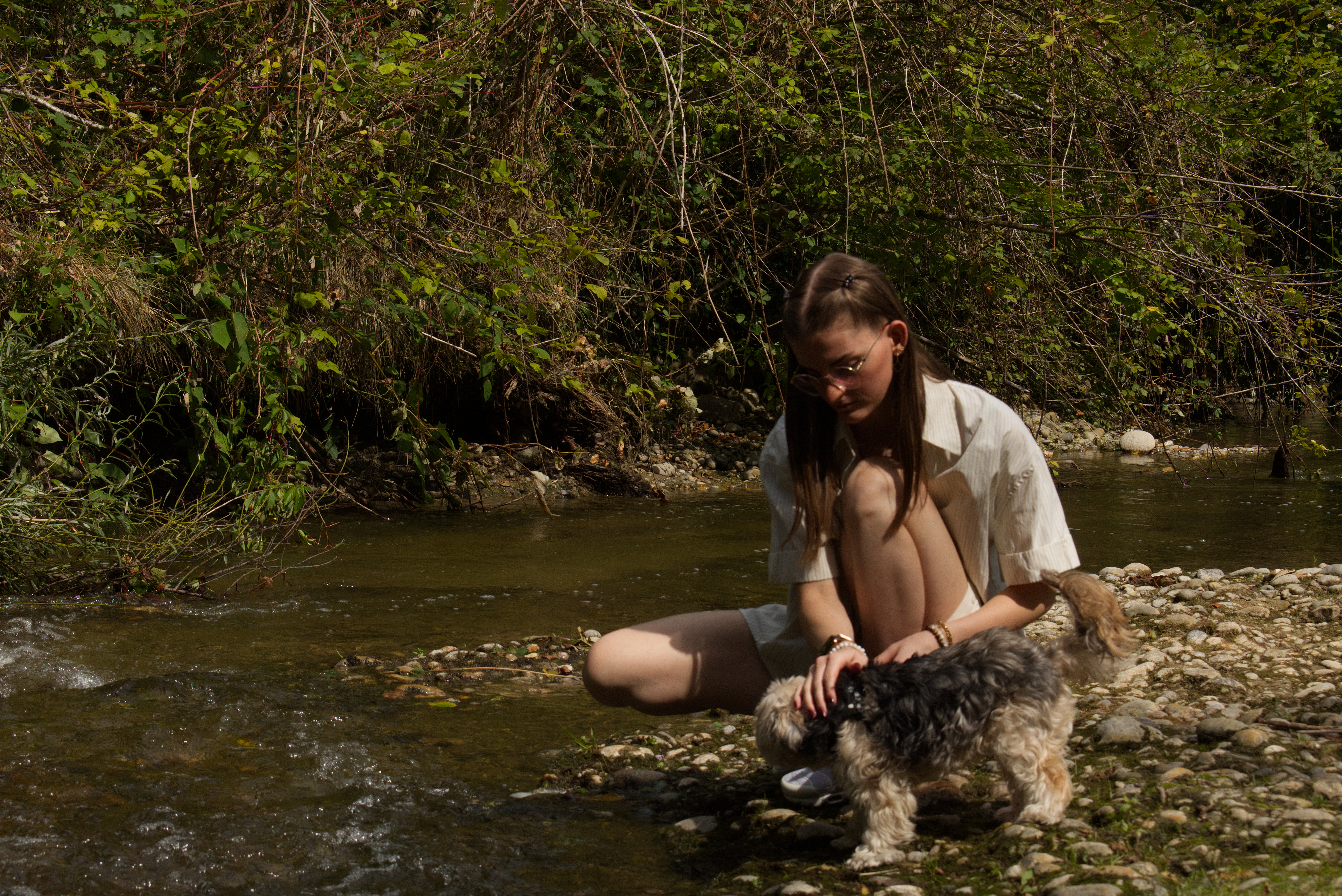 Lisa Karschunke sitzt am Bach und streichelt ihren Hund